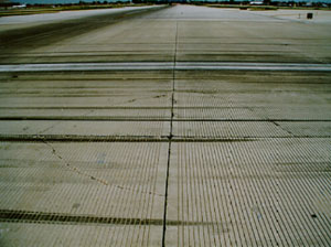 Overview photo showing a corner where four PCC slabs come together.  Three of the four slabs in the photo have low-severity           corner breaks.  Each corner break is a fairly tight, single, non-spalled crack.