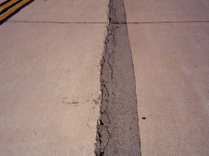 Overview photo of a longitudinal joint with a long narrow asphalt patch along the joint.            The patch is showing visible signs of distress, with spalling and secondary cracking along one side of the patch.