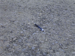 Close-up photo of the pavement surface showing a more significant area of scaling.  In this photo,           the majority of the visible pavement surface looks very pitted.